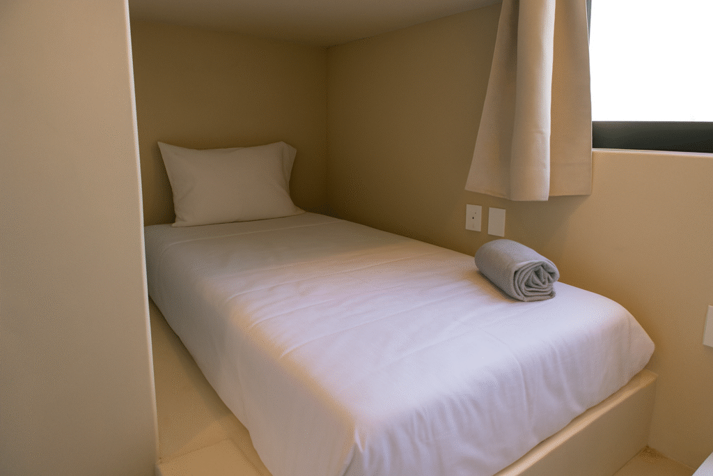 Cama individual en una cápsula privada del Hostal de Samas en La Saladita, con sábanas blancas limpias y toalla.