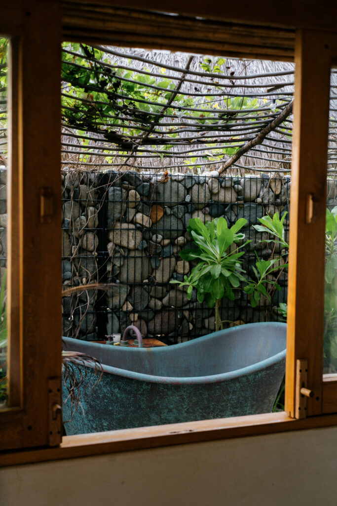 Outdoor bathtub on a private terrace at Samas Hotel La Saladita, surrounded by lush greenery and a stone gabion wall.