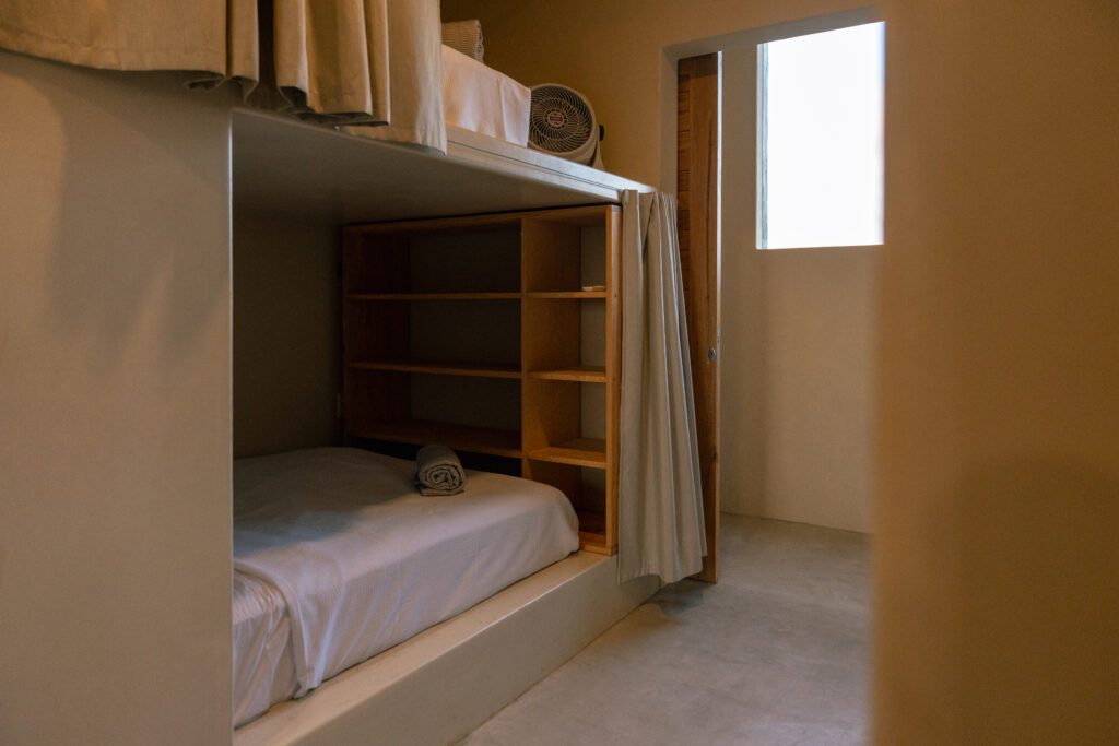 Detail of a capsule-style bunk bed at Samas Hostel La Saladita, showing built-in wooden shelves for storage and privacy curtains.