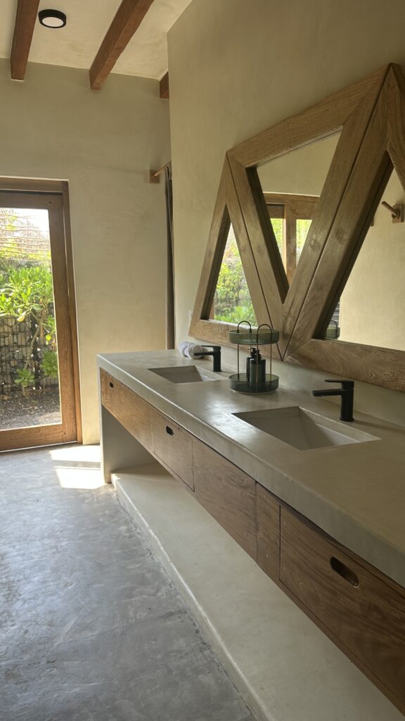 Luxury bathroom at Samas Hotel La Saladita featuring a double vanity, geometric wooden mirror, and access to a private garden.