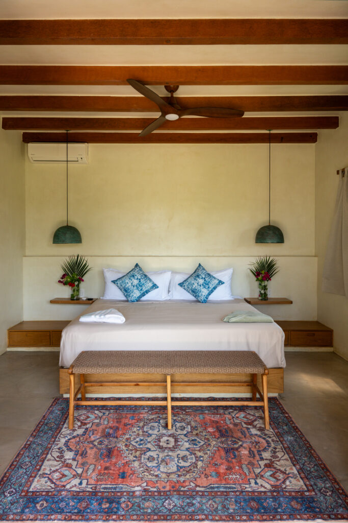 Designer hotel room at Samas La Saladita featuring a king bed, wood beams, a Persian rug, and hanging pendant lights.